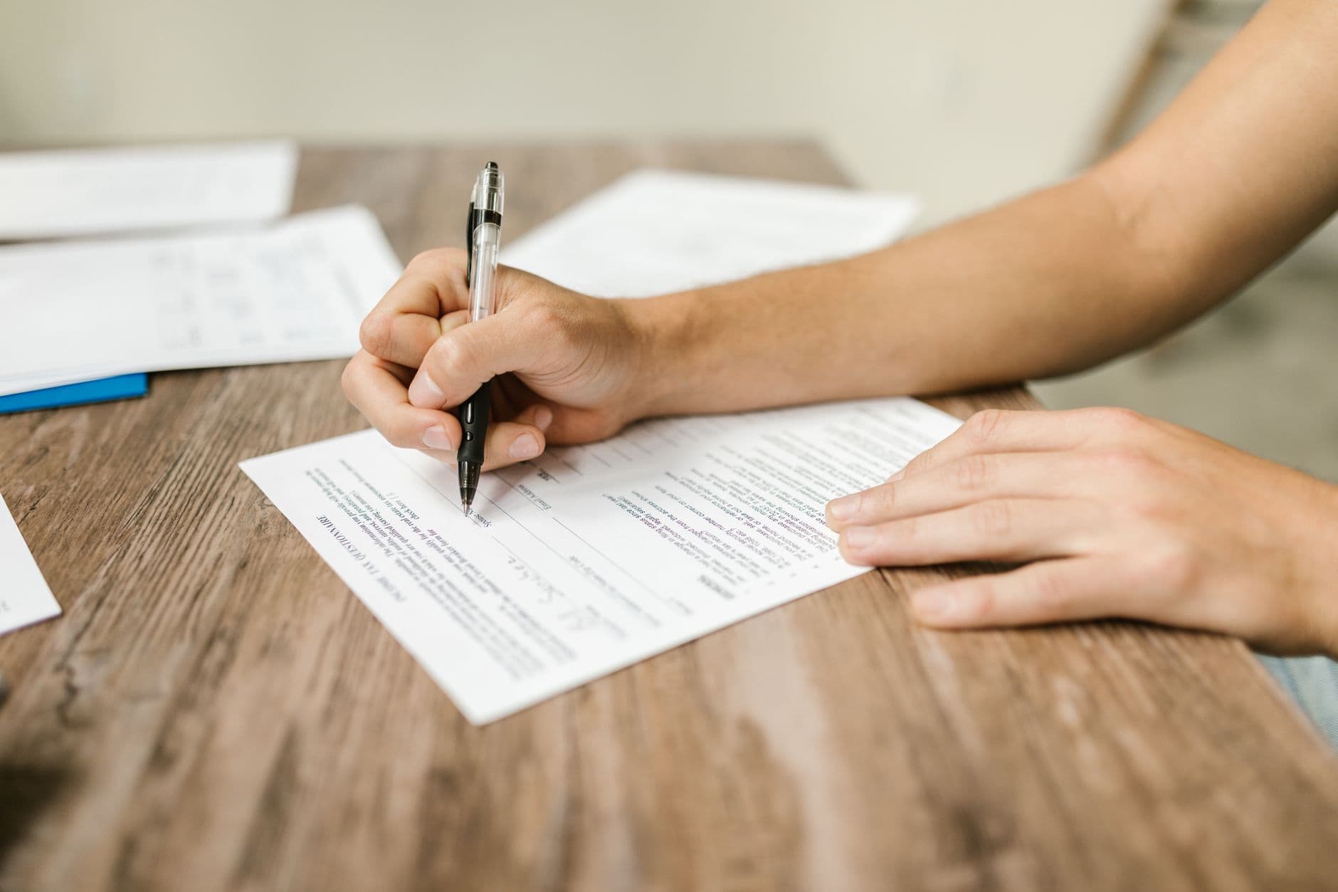 Close-up of a person's hand filling out a paper form with a pen at a desk